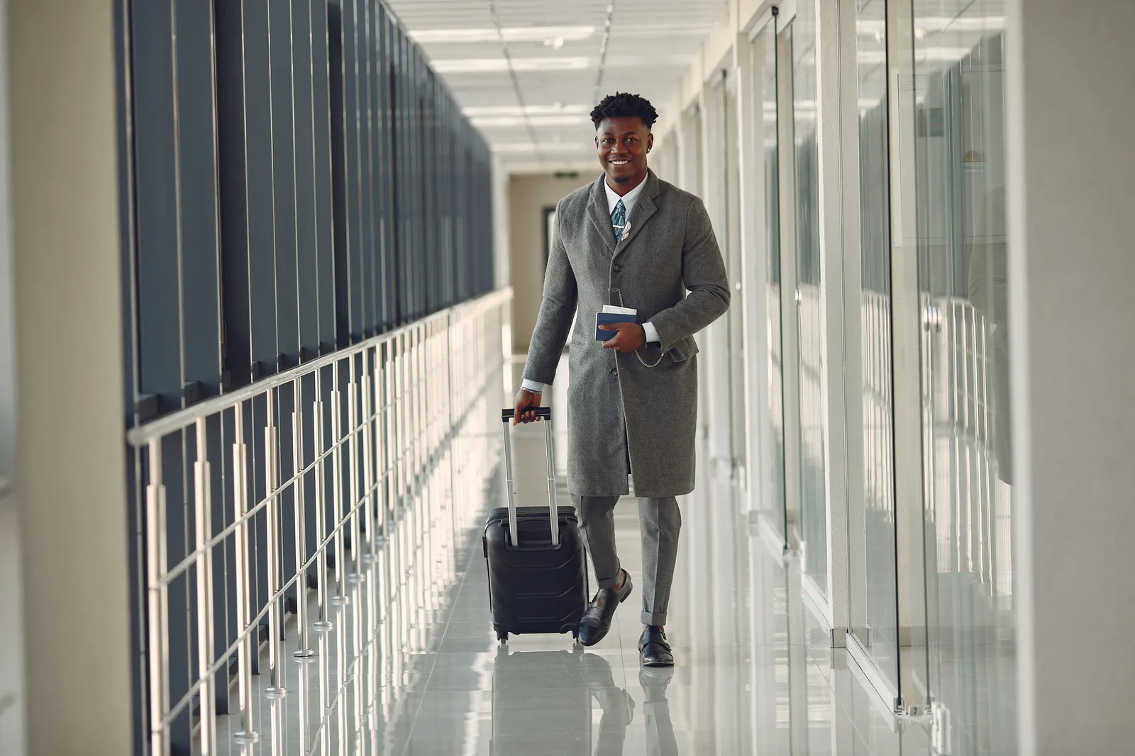 Business executive walking through a modern corridor with a suitcase and passport