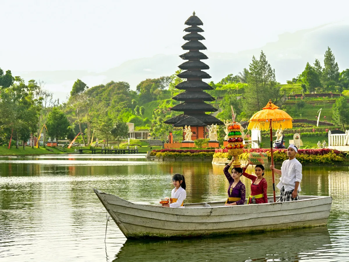 Balinese people in traditional dress carrying offerings on a boat before a tiered temple by a lake in Bali, Indonesia