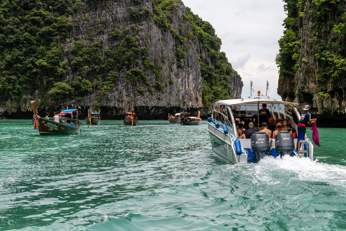 Speedboat and longtail boats among the limestone cliffs and turquoise water of the Phi Phi Islands near Phuket, Thailand