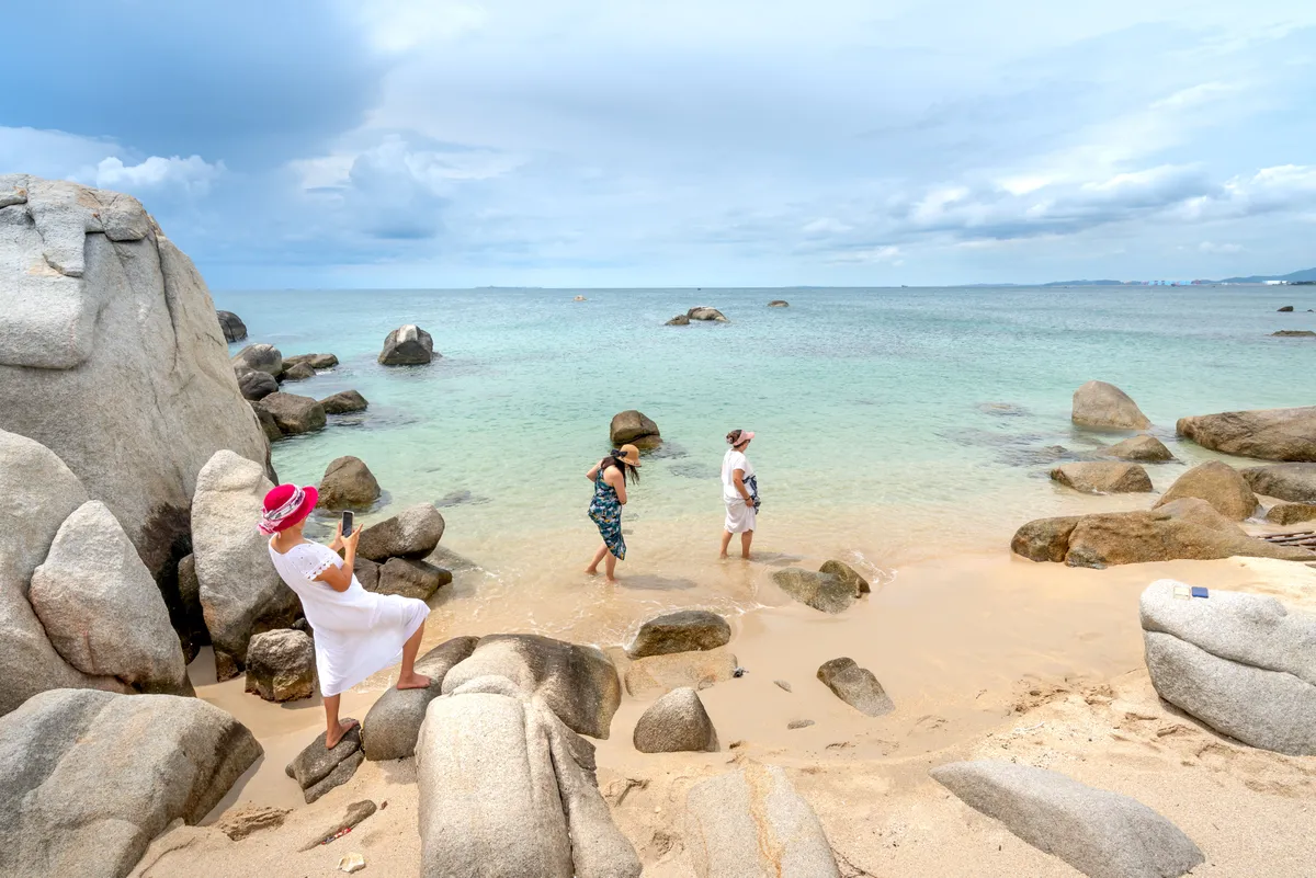 Travellers on a rocky beach with clear turquoise water in Phuket, Thailand