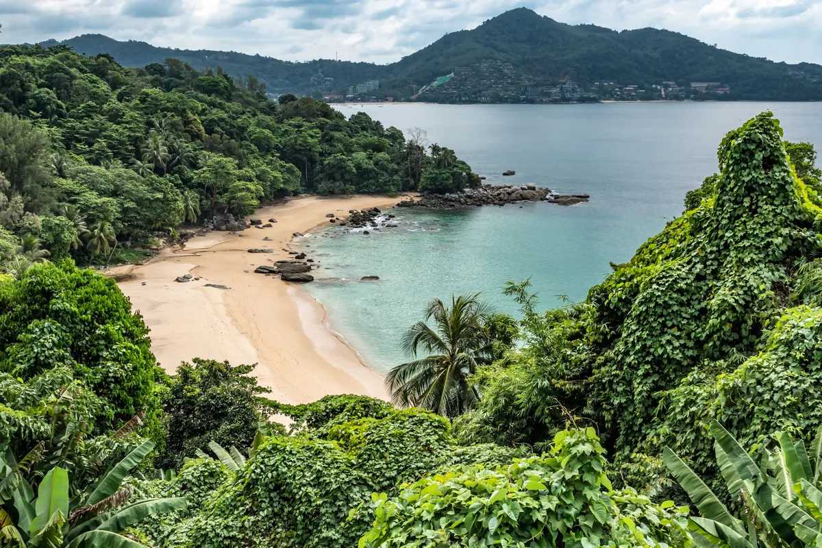 A secluded golden sand cove with turquoise water and green hills on Phuket island, Thailand