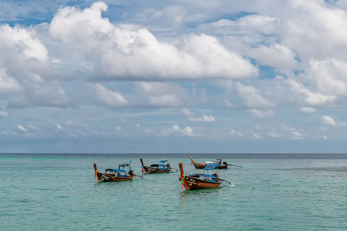 Traditional longtail boats moored in the clear turquoise sea off Phuket, Thailand